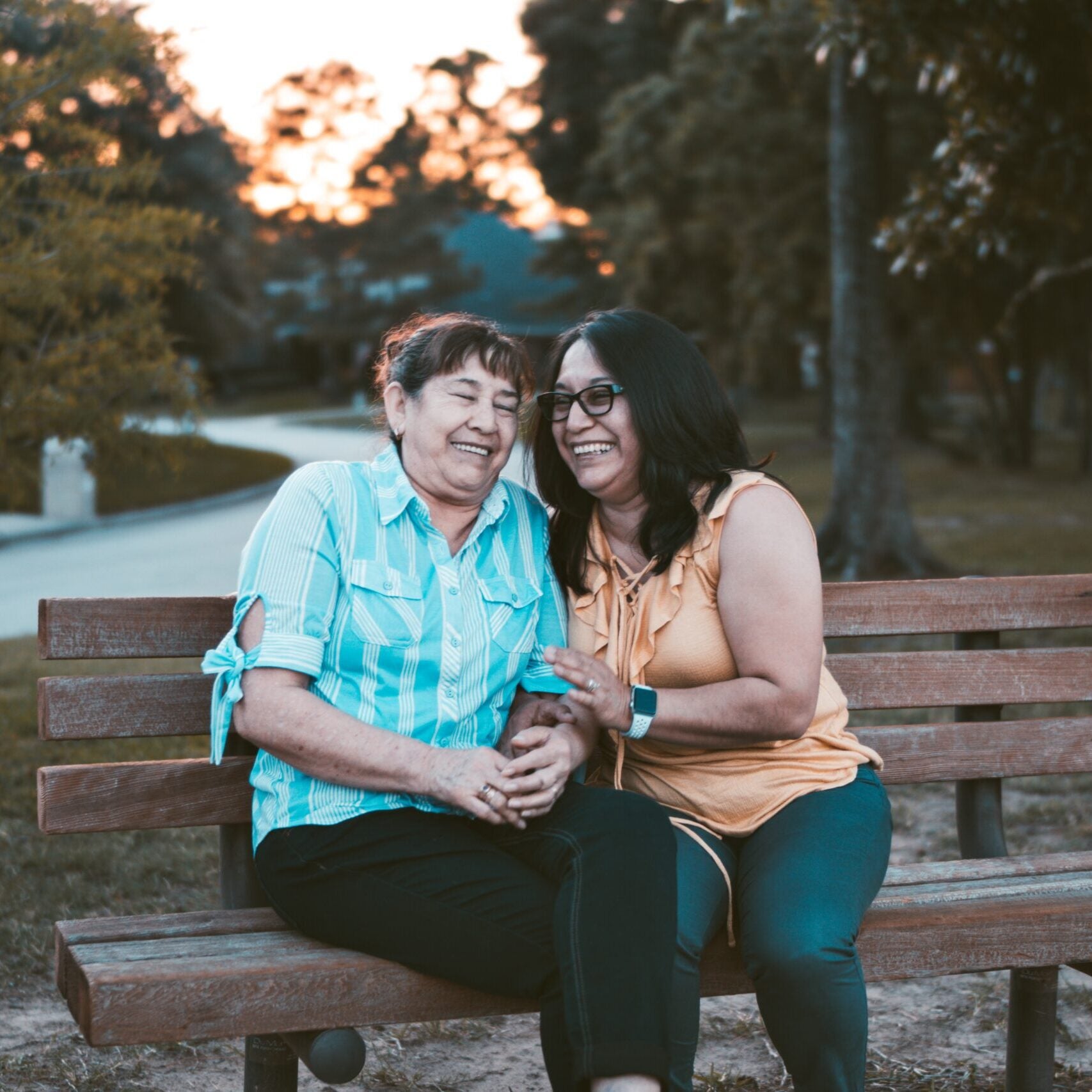 Two Latina women, sharing a laugh on a park bench.