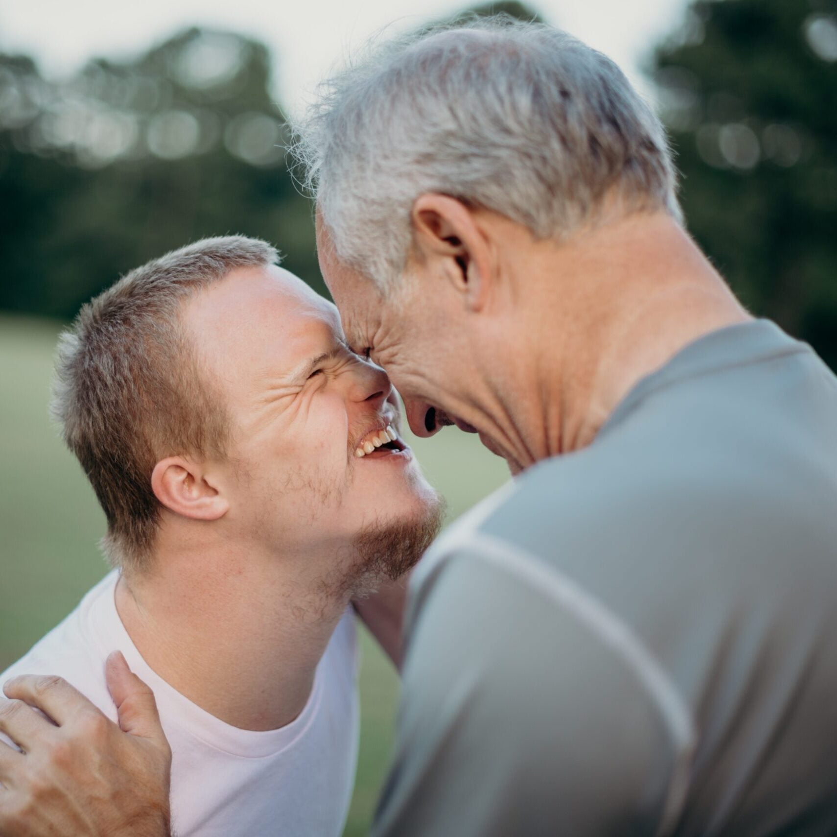 A young man with Down's Syndrome happily greets an older male caregiver.