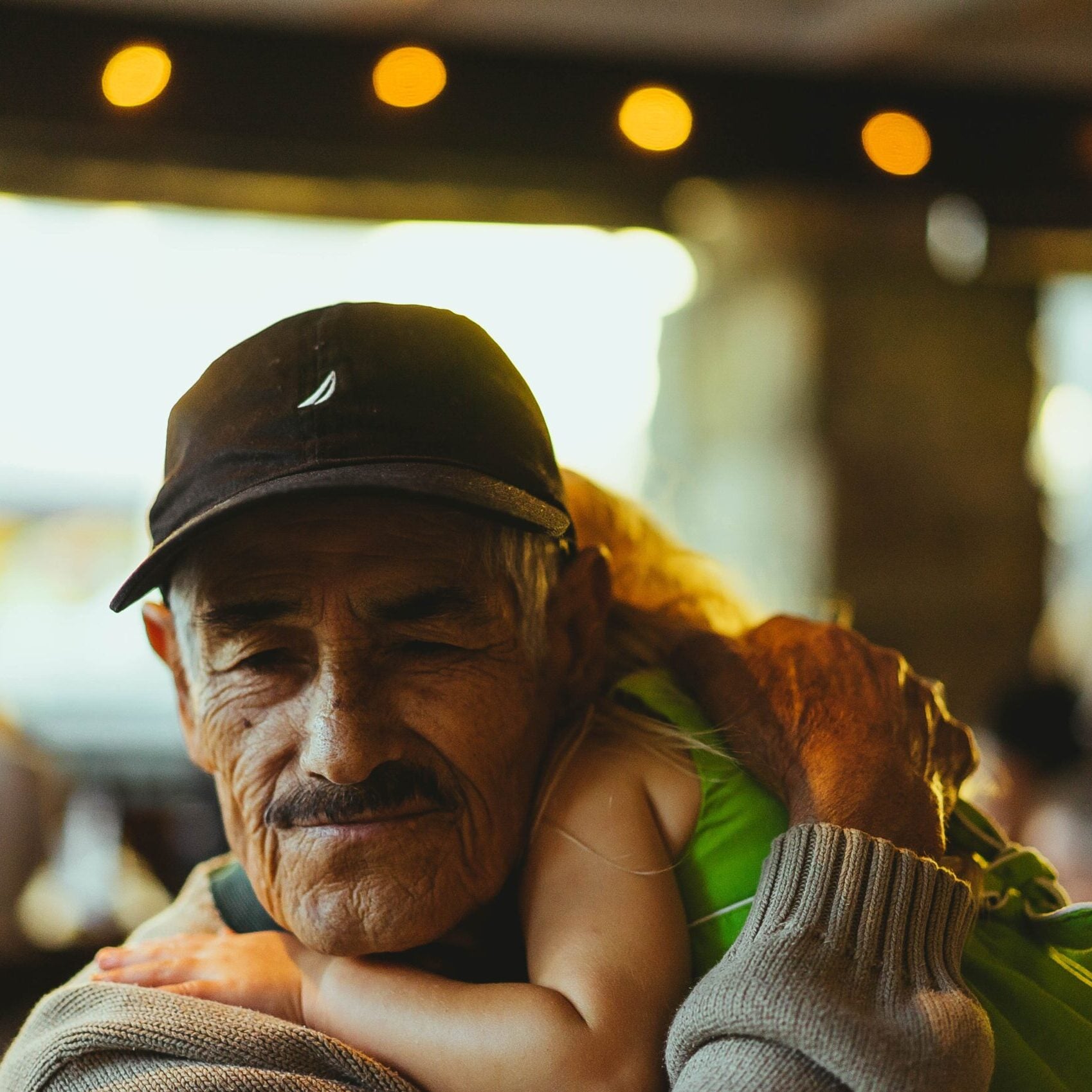 A small child is hugging the neck of an older Hispanic man.