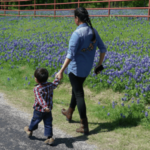 Mother and child holding hands while strolling past a lush field of bluebonnets.